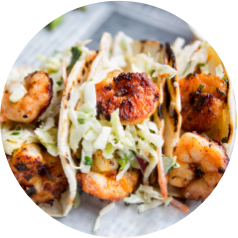Grilled shrimp tacos topped with shredded cabbage and fresh herbs on a plate.