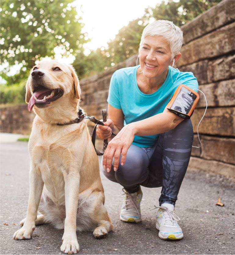 Senior person with short hair crouches and holds a leash attached to a happy dog during a walk.