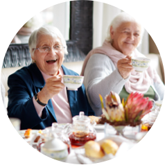 Two senior women enjoying tea together at a beautifully set table with smiles and raised teacups.