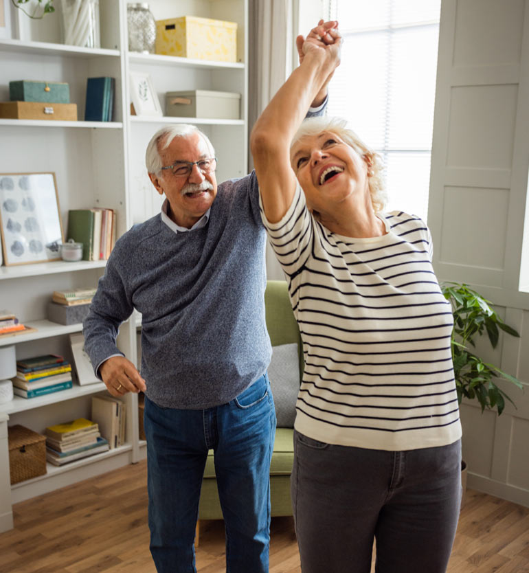An elderly couple joyfully dancing together in a bright and cozy living room.