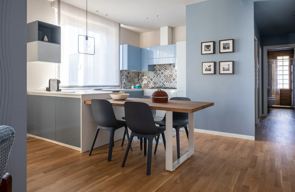 Modern kitchen and dining area with light blue cabinets, wooden floor, and wall decor.