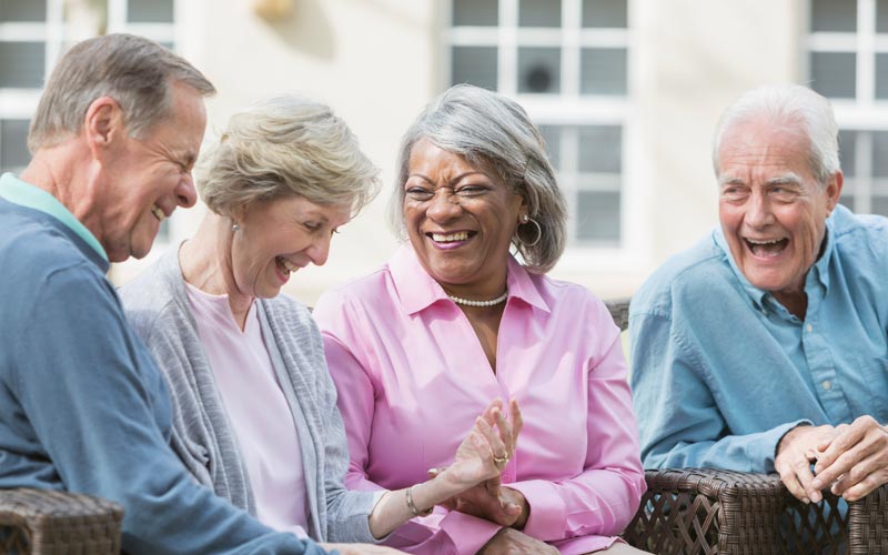 Four senior adults laughing and having a conversation while sitting outdoors