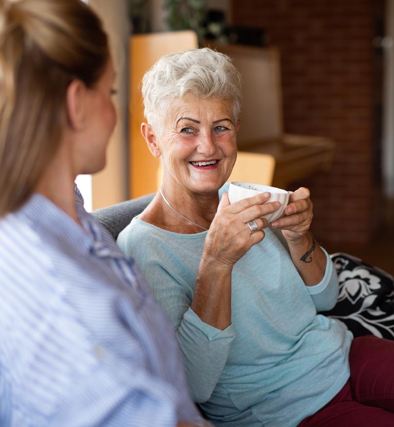 Senior woman smiling while chatting with a team member during a relaxed meeting over coffee.