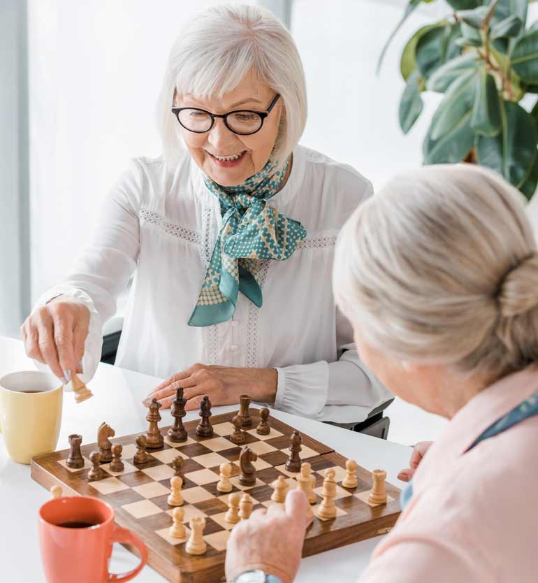 Two senior women playing chess together at a table, enjoying each others company.