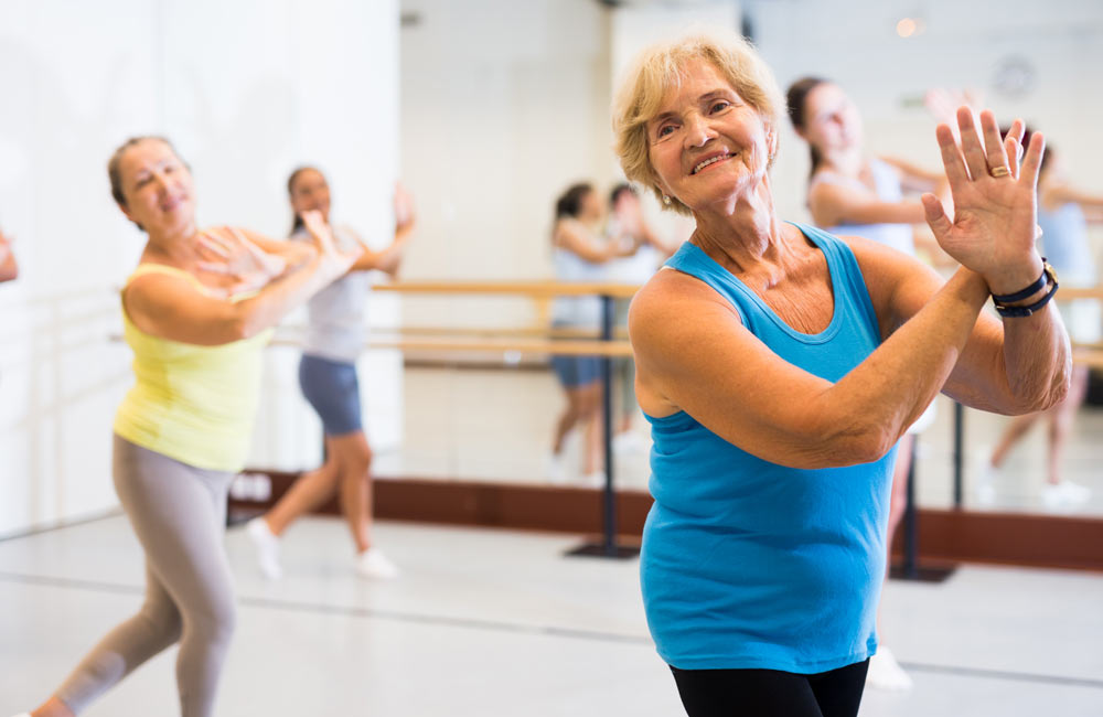 Older women participating in an exercise class, smiling and performing dance movements.
