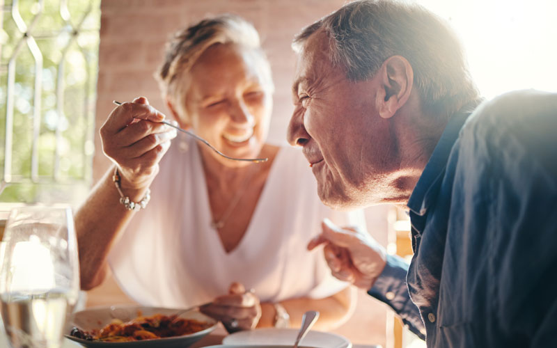 Senior couple laughing and feeding each other at a restaurant.